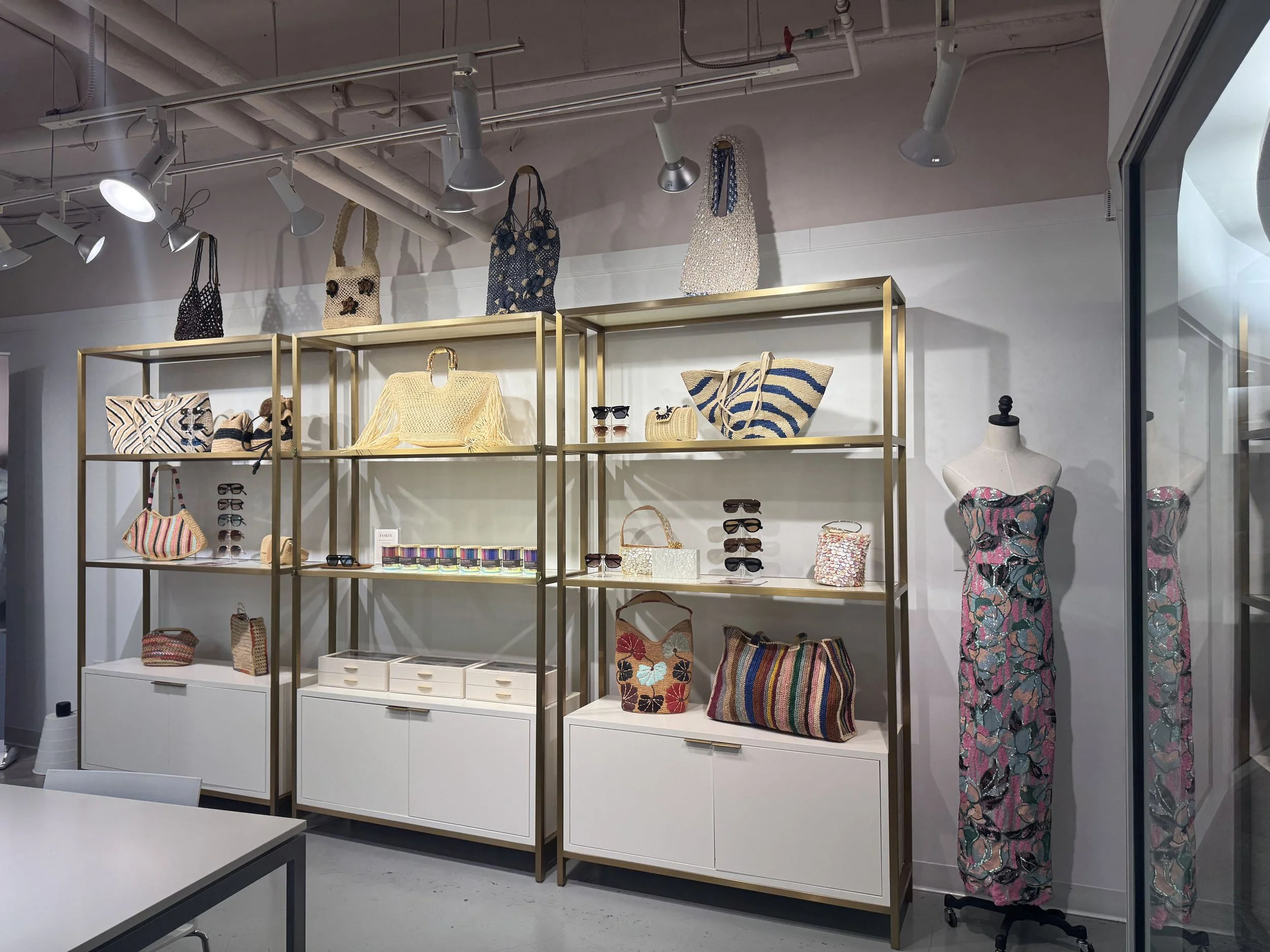Display of fashionable accessories including handbags, sunglasses, and jewelry, with striped clothing on a mannequin, in a retail store with overhead track lighting.