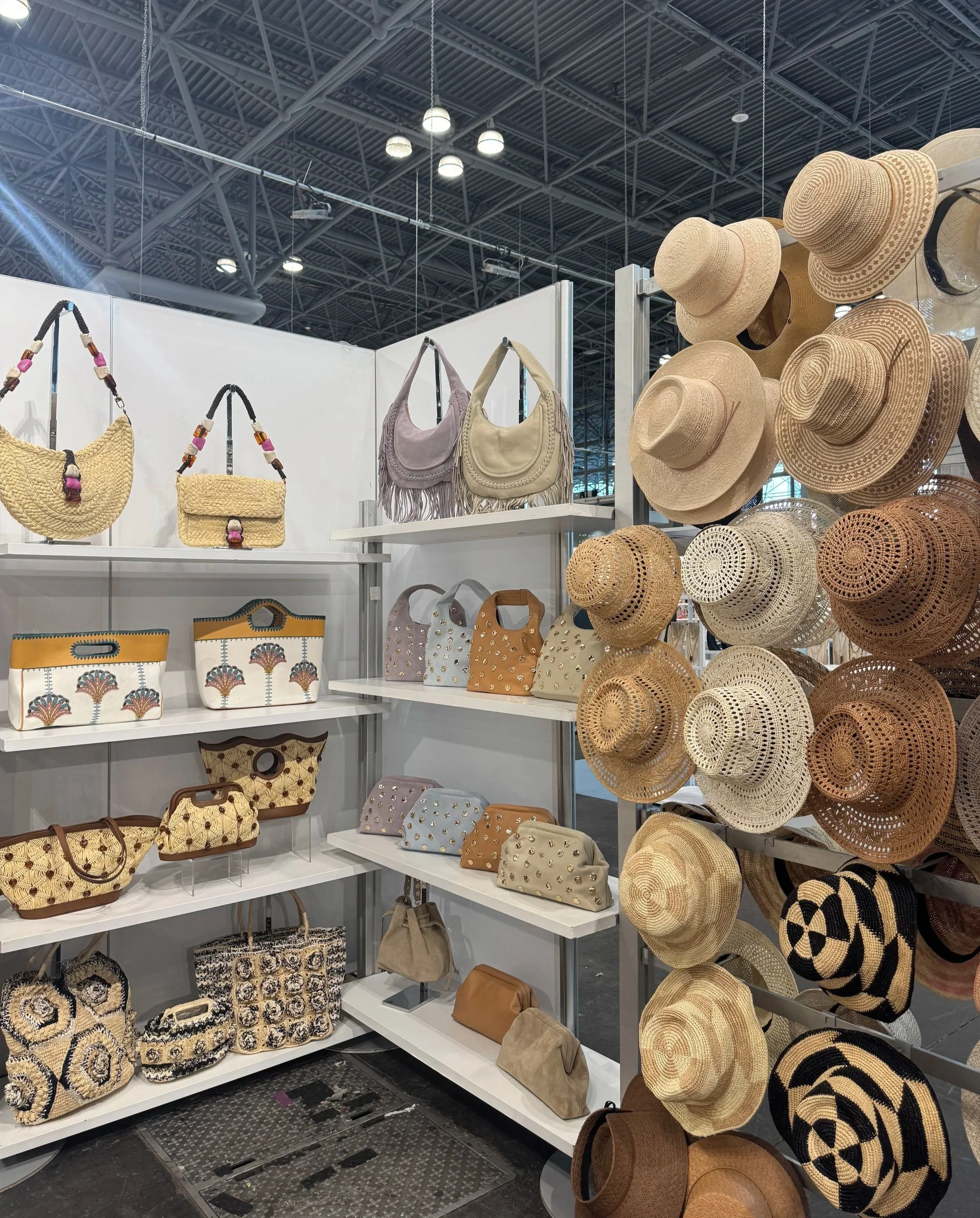 Display of beige and straw-colored wide-brimmed hats hanging on the right side of a retail display shelf. To the left, there are white shelves with handbags in pastel colors, some decorated with fringe or embroidery patterns, at an indoor shopping mall.