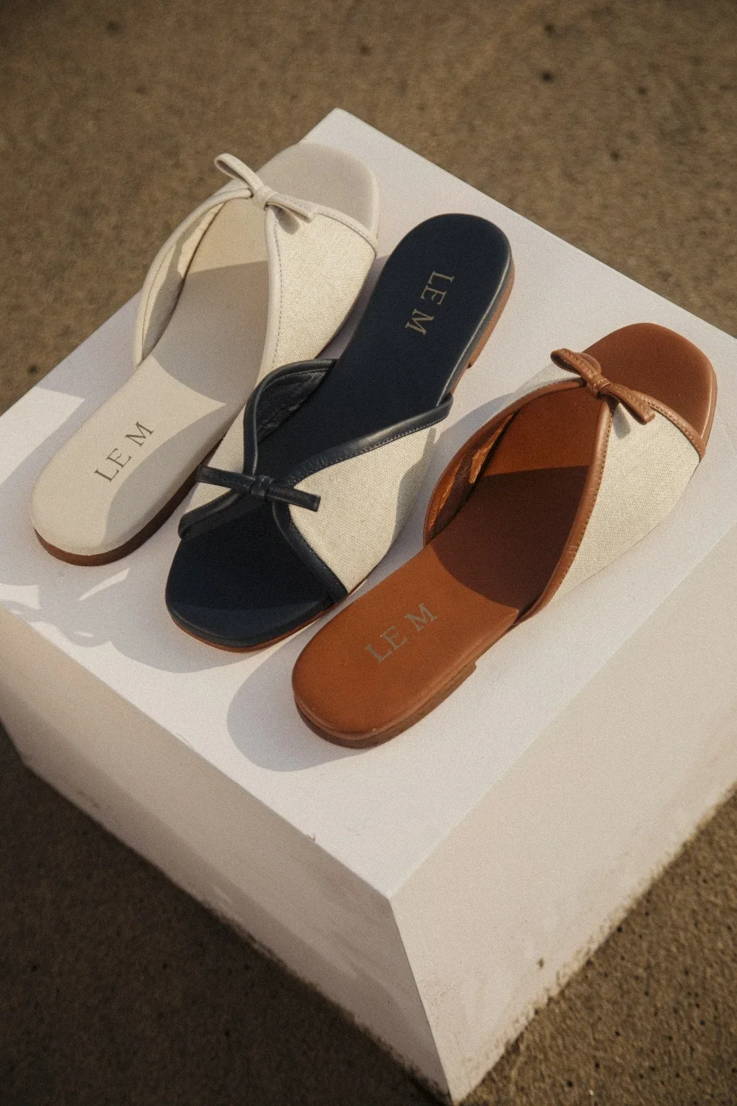 Three pairs of open-toe sandals with ankle straps in white, black, and brown, placed on a white surface.