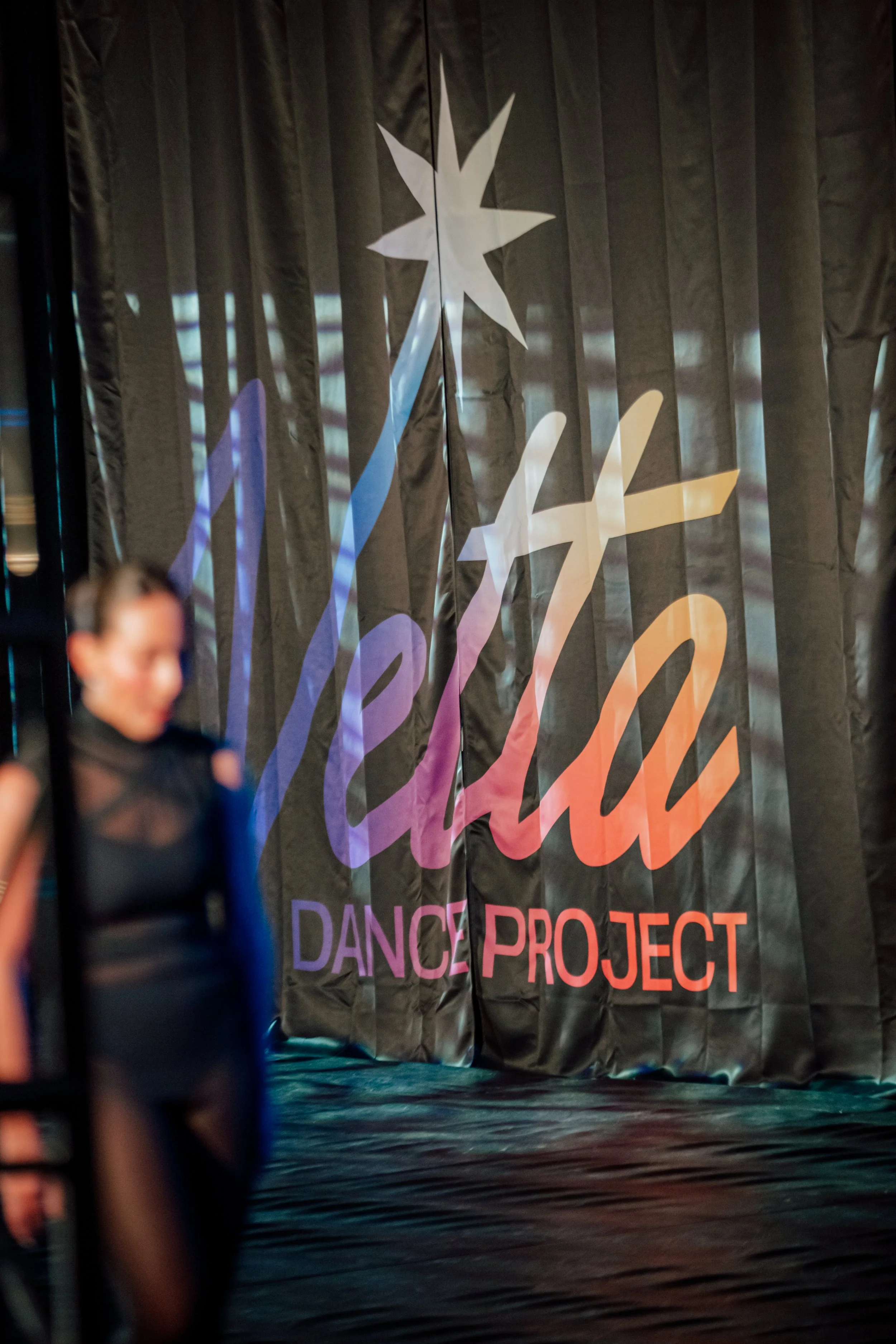 Stage with black curtain and colorful sign reading 'Dance Project'. Blurred person in the foreground.