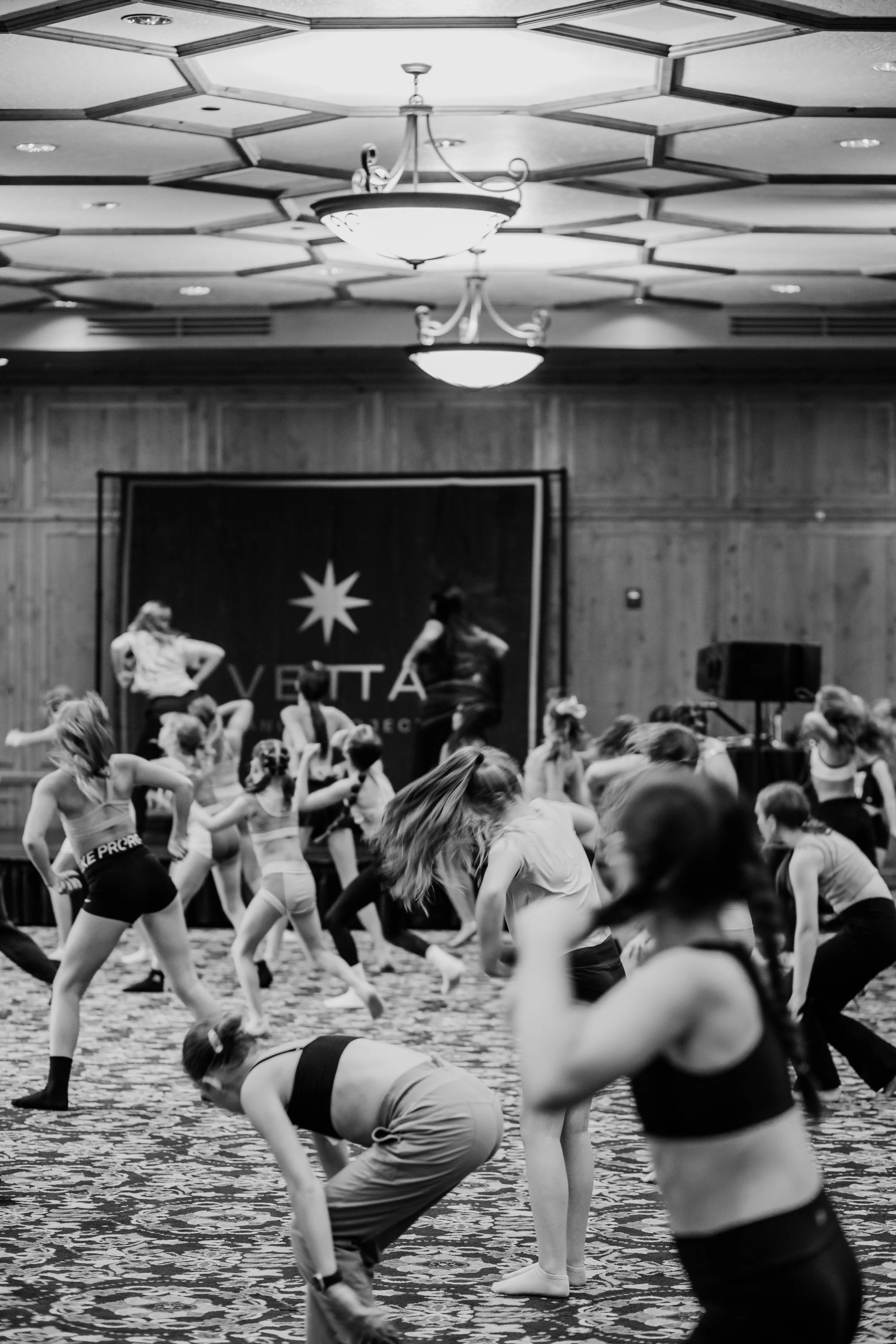 Dance studio with young dancers practicing in preparation for a performance with banners and lighting fixtures on the ceiling.