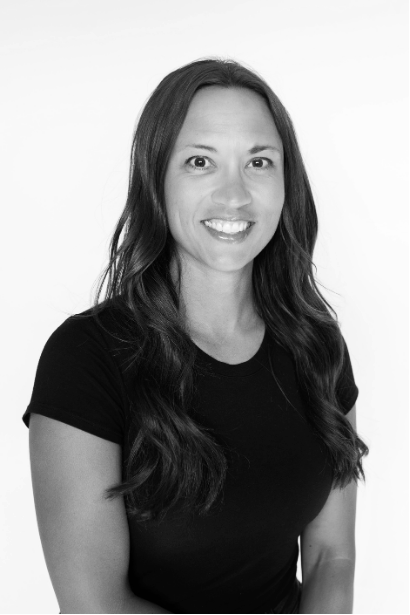 Black and white portrait of a woman with long wavy hair, smiling, wearing a black short-sleeve shirt, against a plain background.