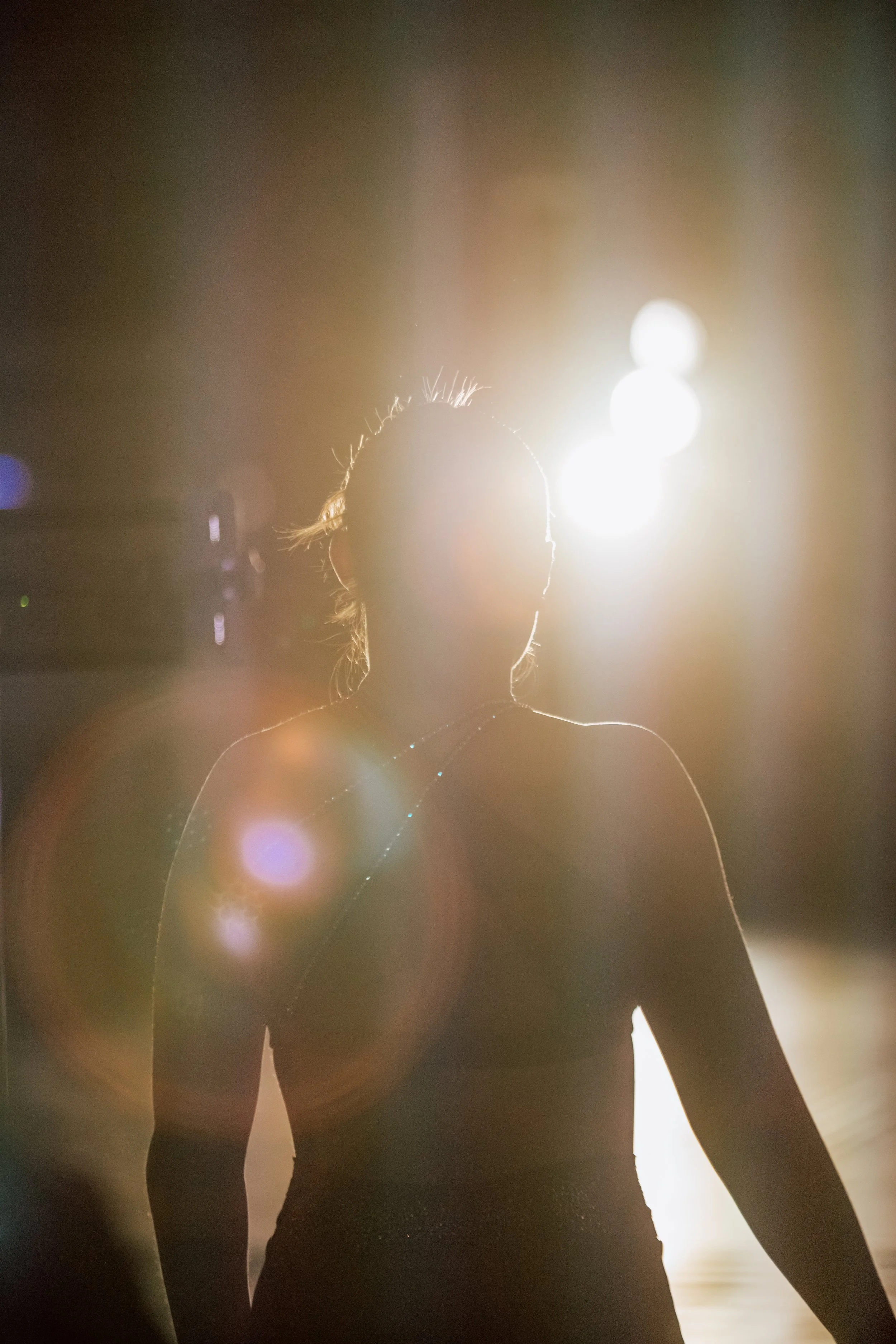 Silhouette of a woman in a sports bra and shorts standing in front of bright sunlight, creating a lens flare effect.