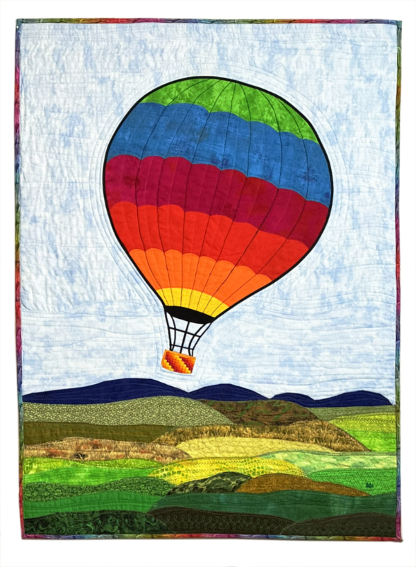 Colorful quilt depicting a hot air balloon ascending over a landscape of rolling hills and fields.