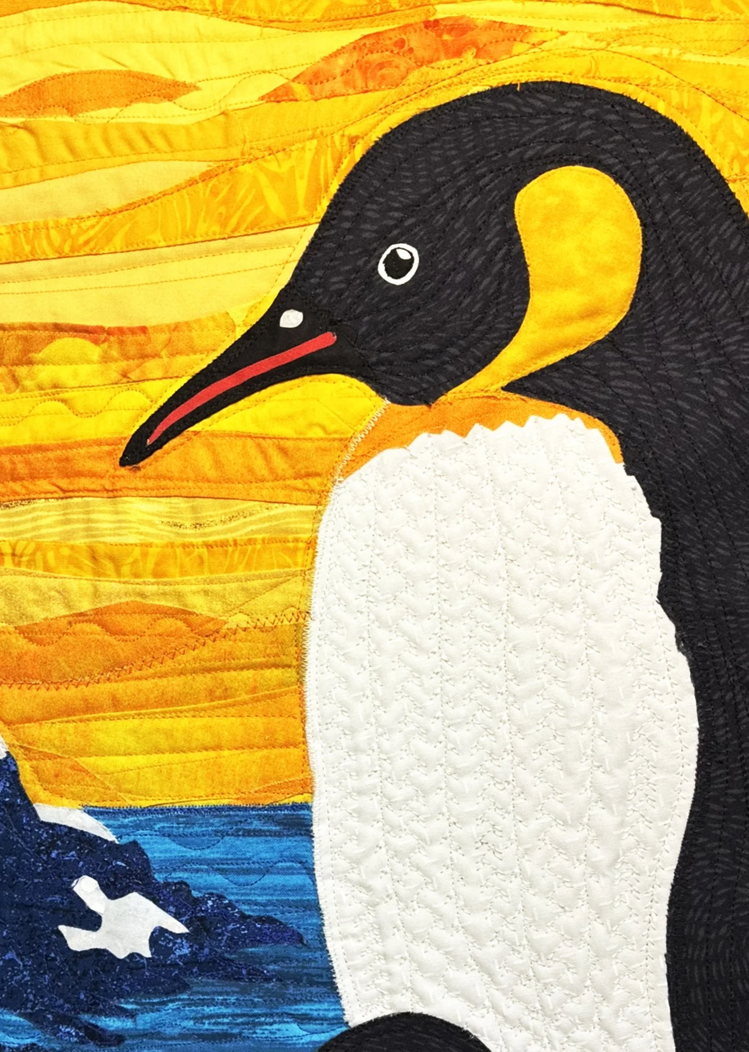 Close-up of a quilted textile featuring a stylized image of a bird, possibly a penguin, with a background of vibrant orange and yellow hues resembling a sunset or sunrise.