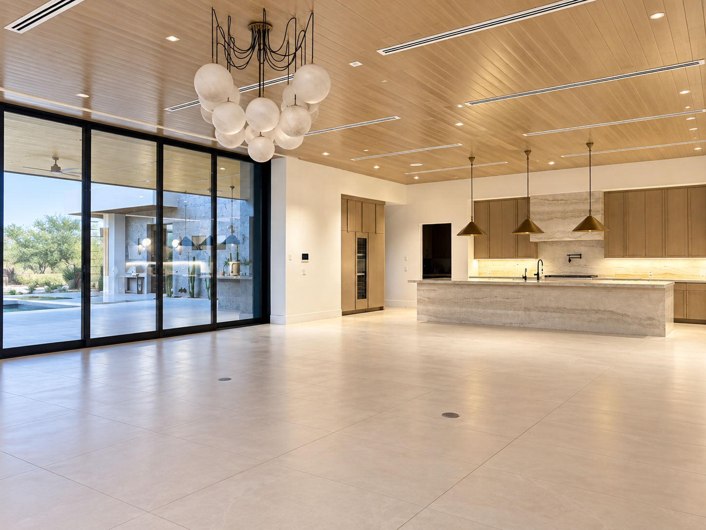 Modern open-plan kitchen and living area with wooden ceiling, large sliding glass doors, hanging light fixtures, and minimalistic design.