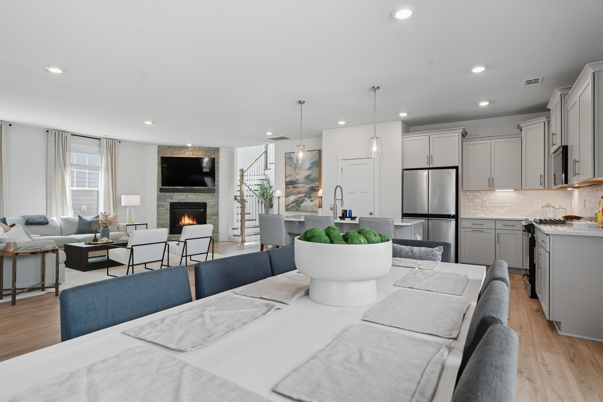 Open-concept living room and kitchen with white cabinetry, stainless steel refrigerator, fireplace, wall-mounted TV, and modern decor.