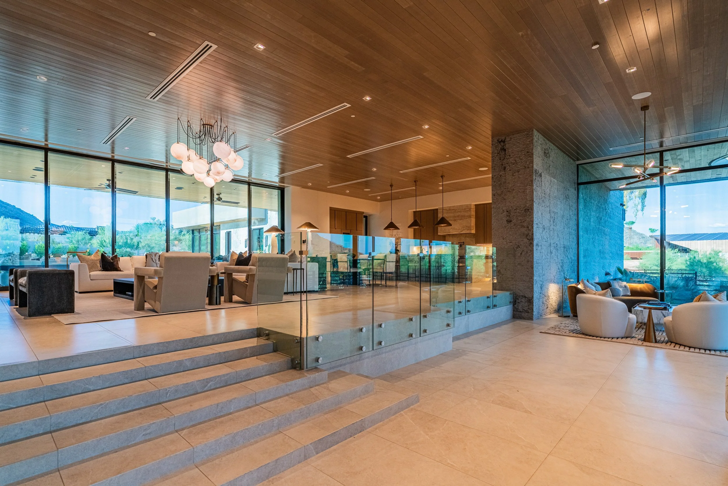 Modern open-concept lobby or lounge with large windows, wooden ceiling, and stylish lighting fixtures. Comfortable seating areas with sofas and chairs, and a view of outdoor landscape.