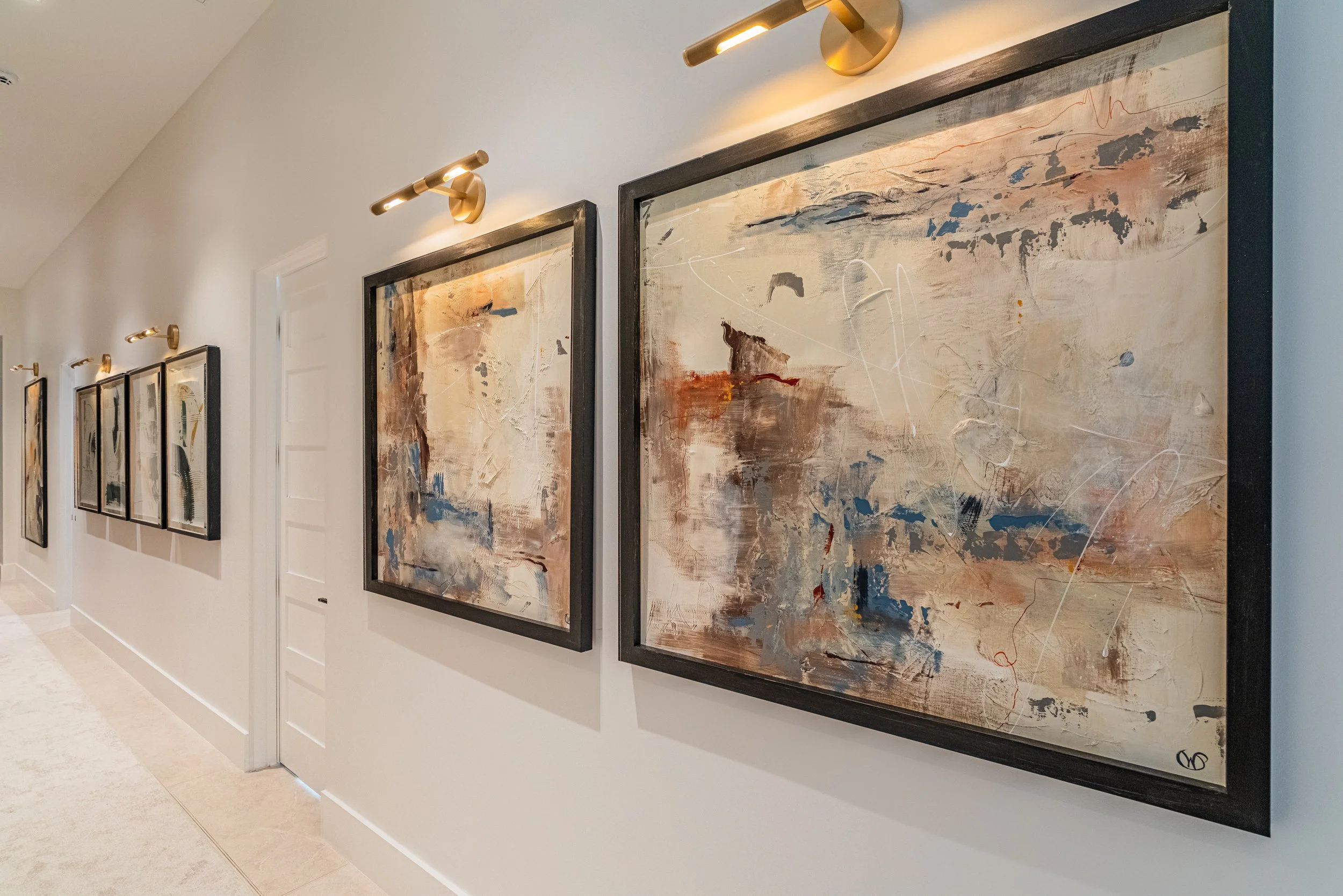 Gallery wall with abstract paintings illuminated by adjustable wall-mounted lights in an art gallery or modern interior.