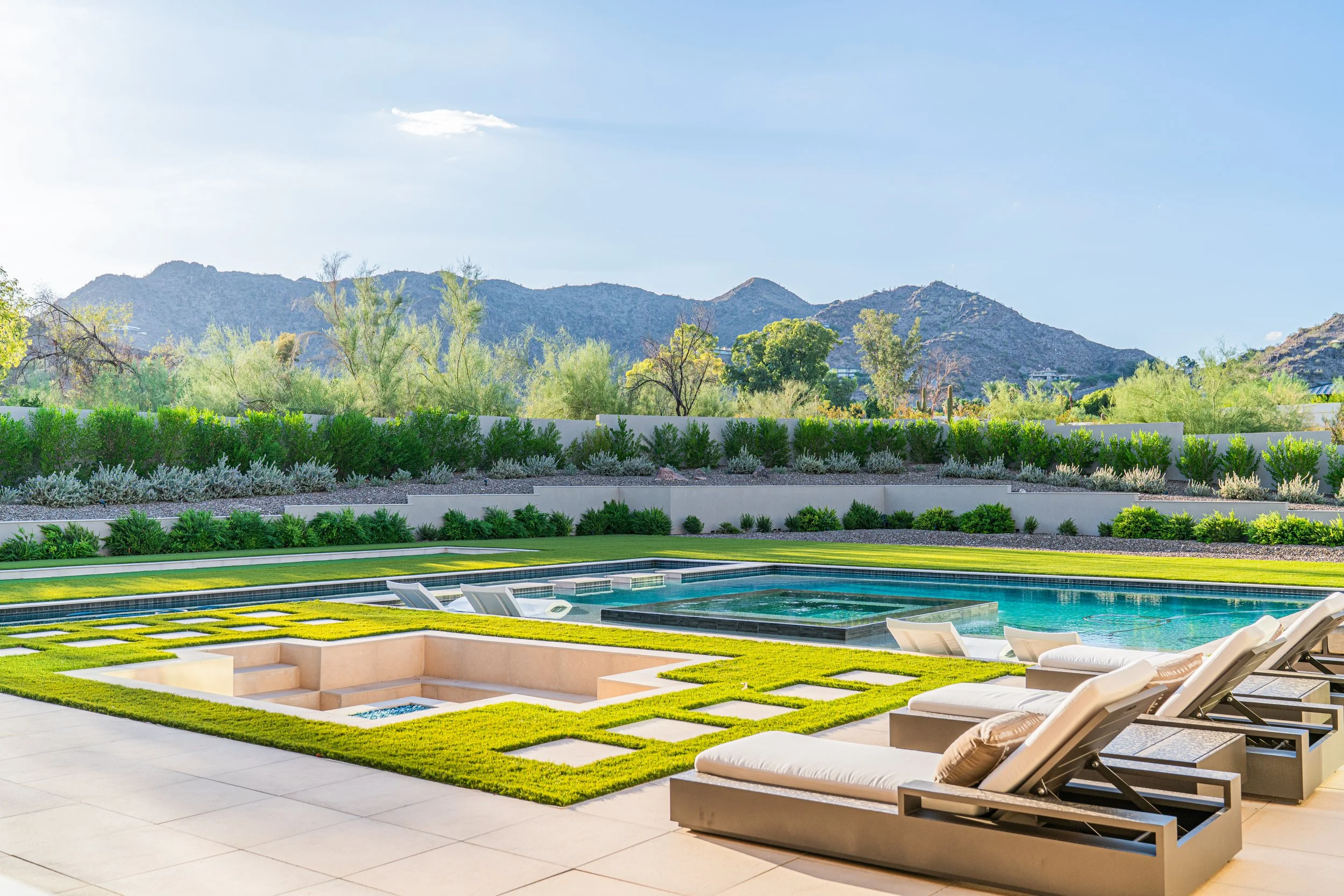 Luxury backyard with swimming pool, sun loungers, green lawn, and landscaped garden with mountains in the background.