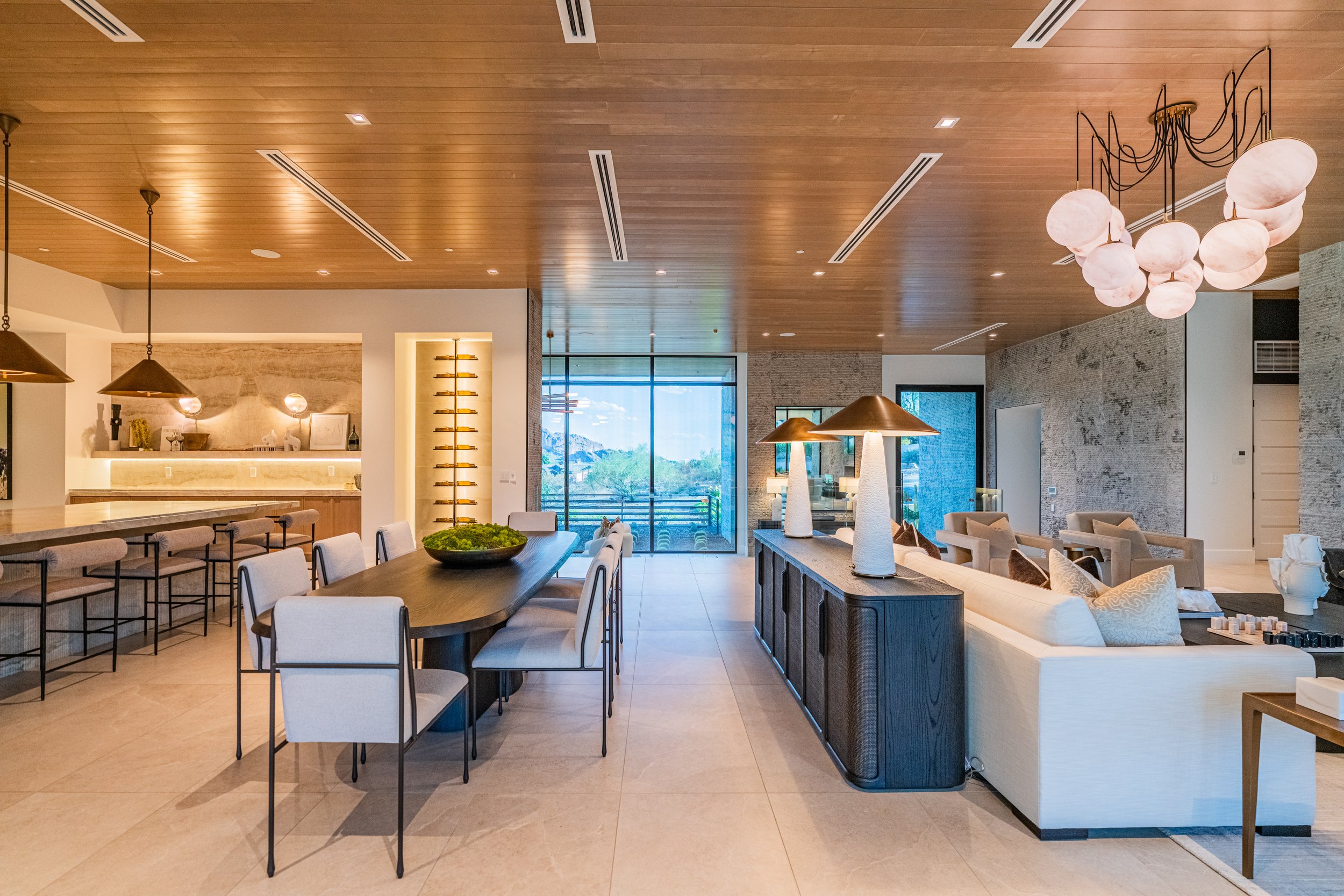 Modern open-concept living and dining area with wooden ceiling, large window, chandelier, and contemporary furniture.