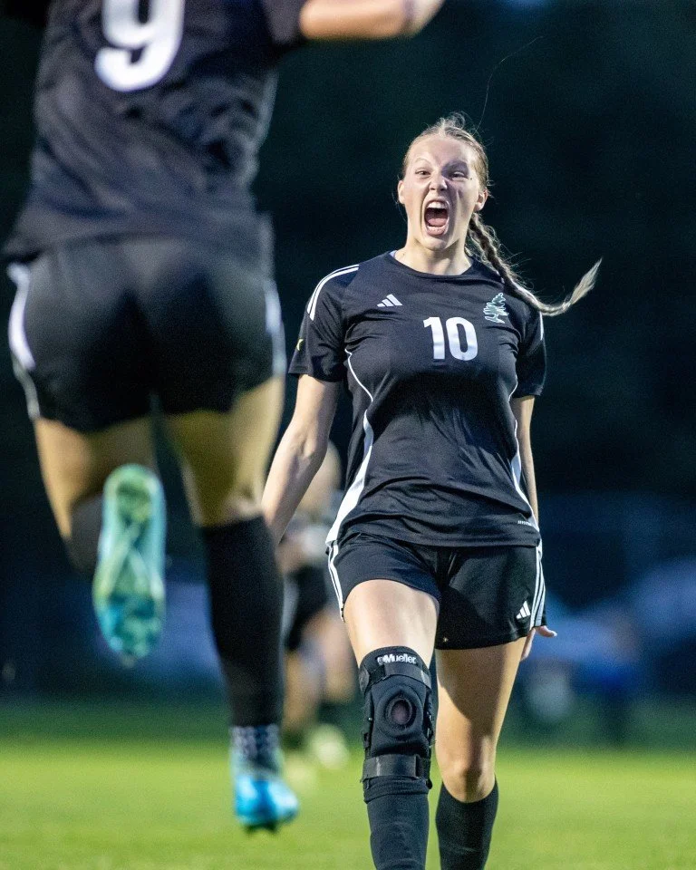 An intense moment during a soccer game featuring a female player in a black uniform with the number 10, wearing a knee brace, celebrating on the field.