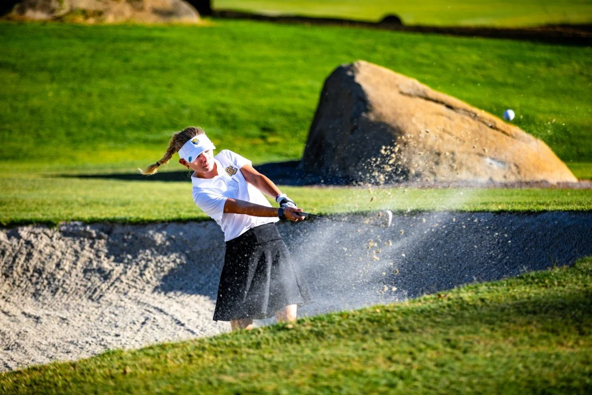 Female golfer hitting a golf ball from a sand bunker at a golf course.