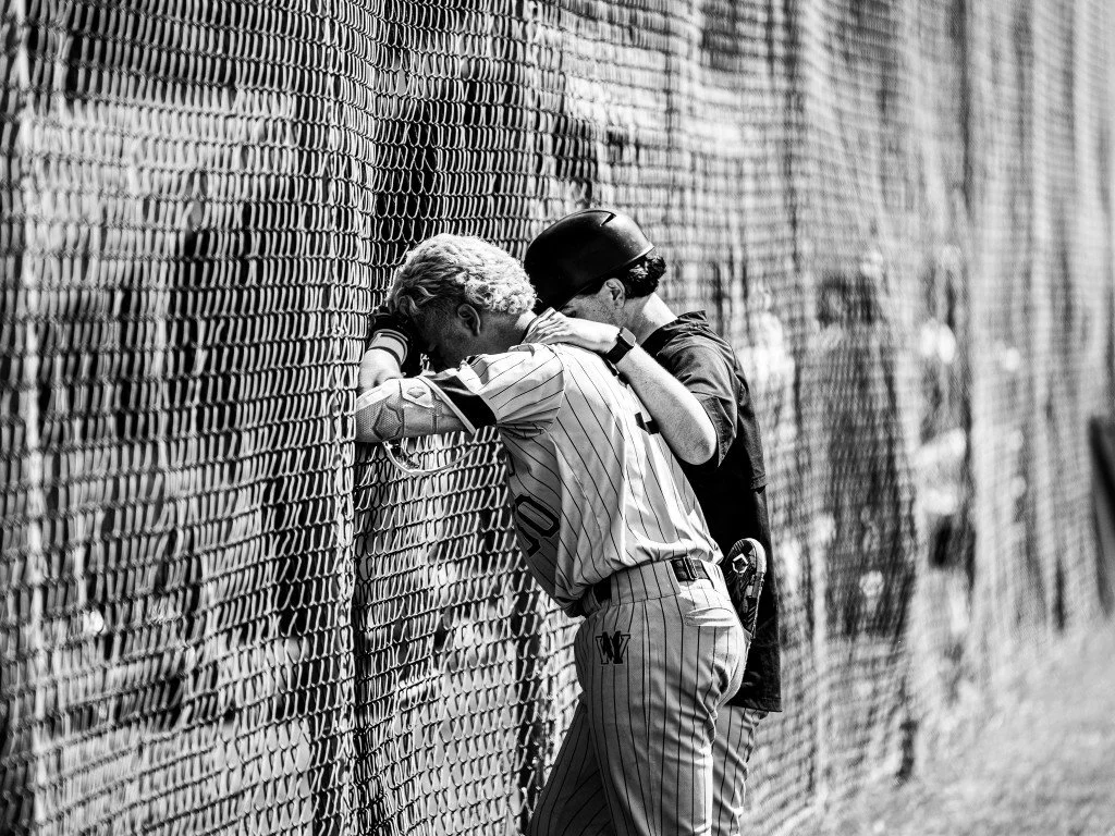A baseball player and a police officer sharing a moment by a chain-link fence.