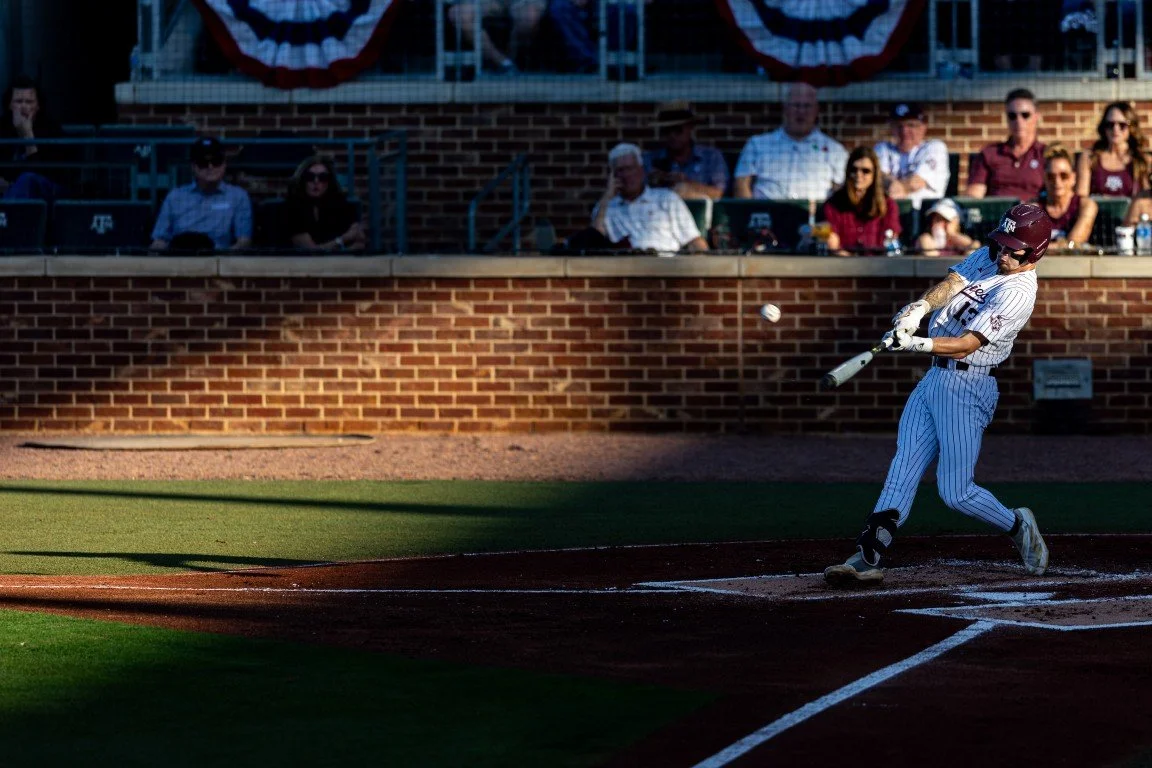 Baseball player swinging at a pitched ball during a game, with spectators seated in the background.