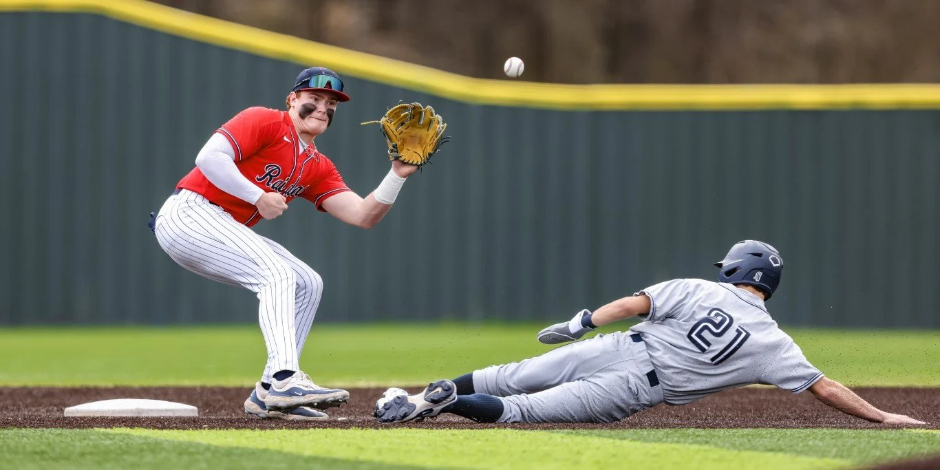 A baseball player in a gray uniform with the number 21 slides into a base as another player in a red uniform with a baseball mitt attempts to catch the ball.