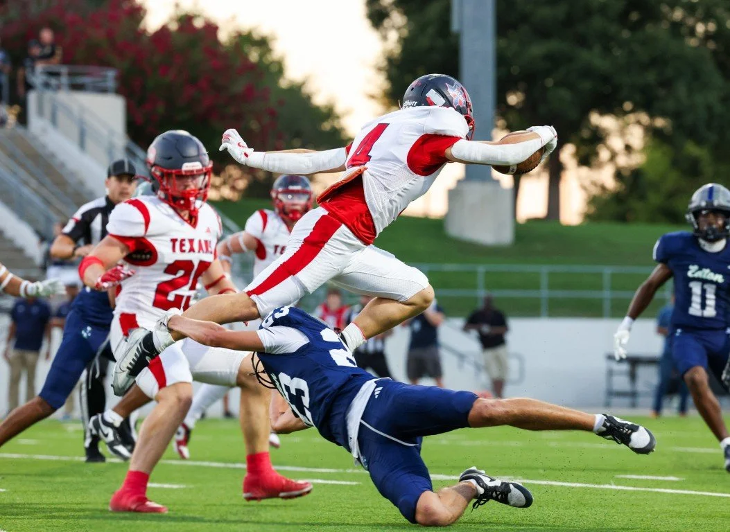 American football players in action during a game, with one player leaping over another.