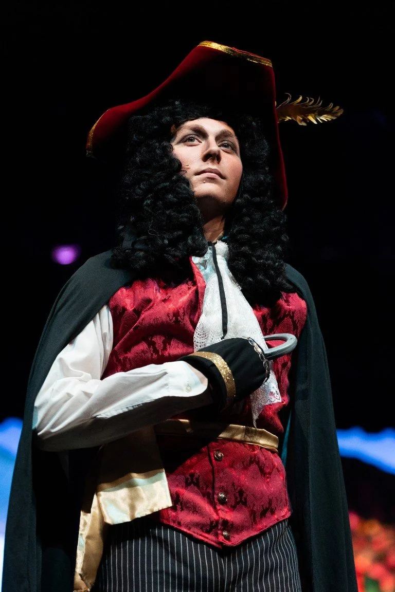 A woman dressed in a pirate costume, with a red coat, white shirt, black cape, and a large red hat with a feather, holding an umbrella.