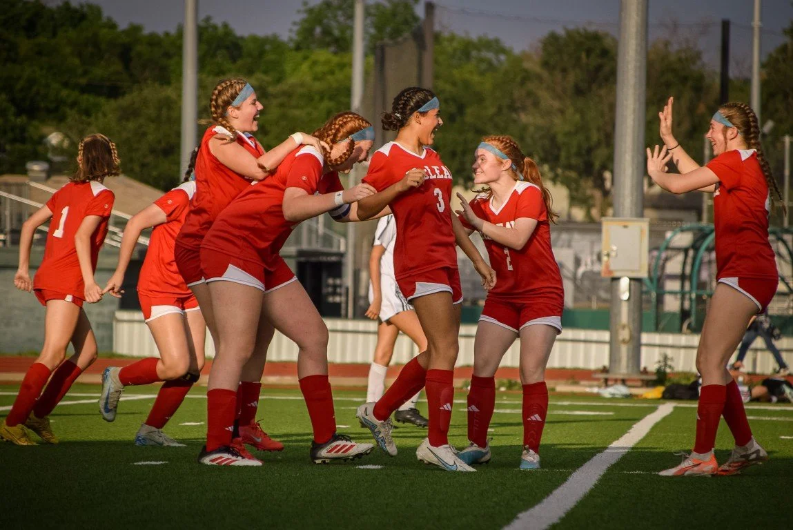 Group of female soccer players celebrating on the field in red uniforms.