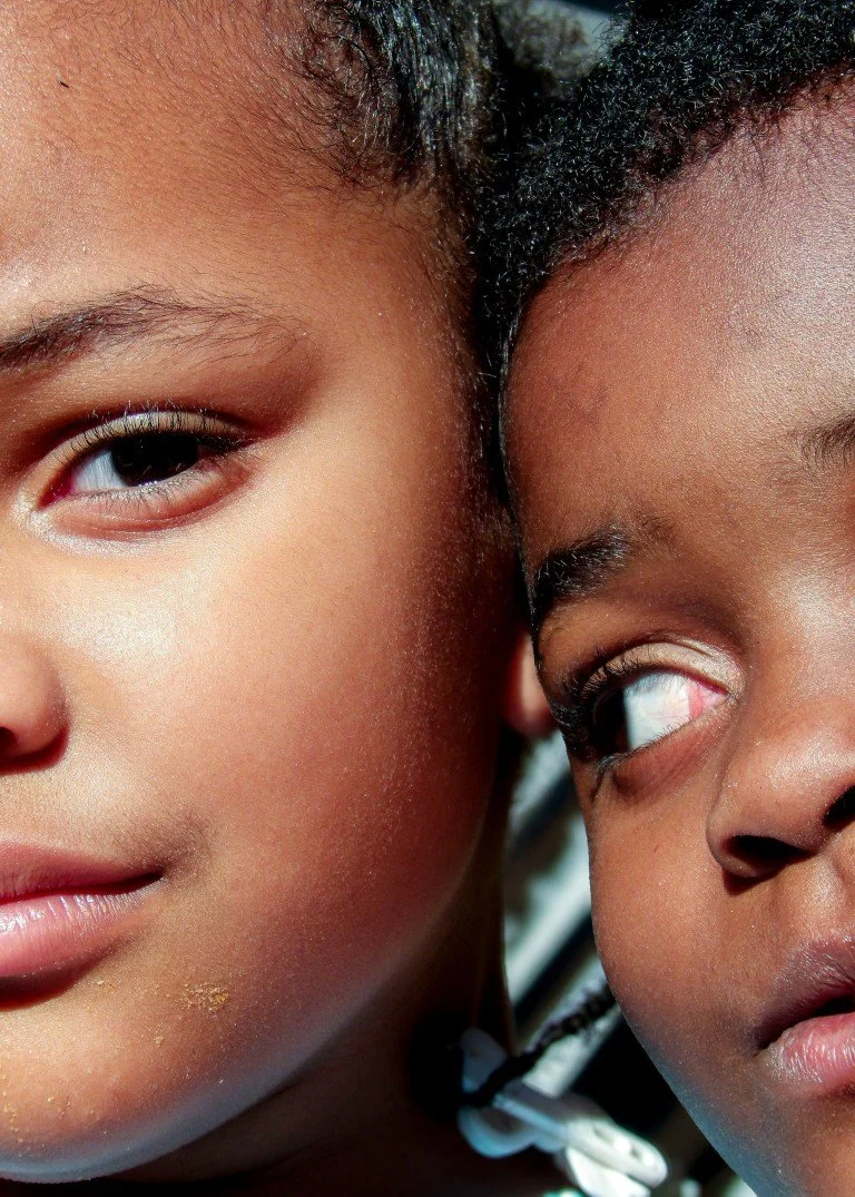 Close-up of two children with dark skin, one smiling and the other looking at the first.