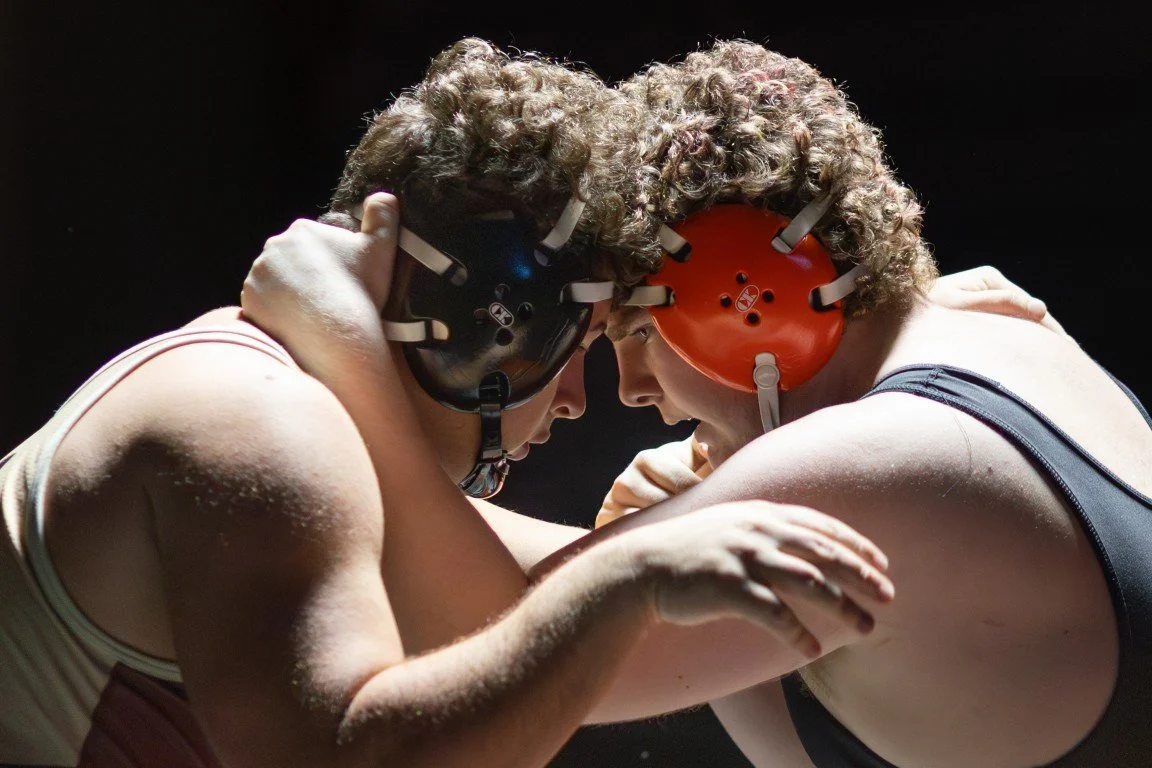 Two wrestlers in helmets wrestling on a mat.