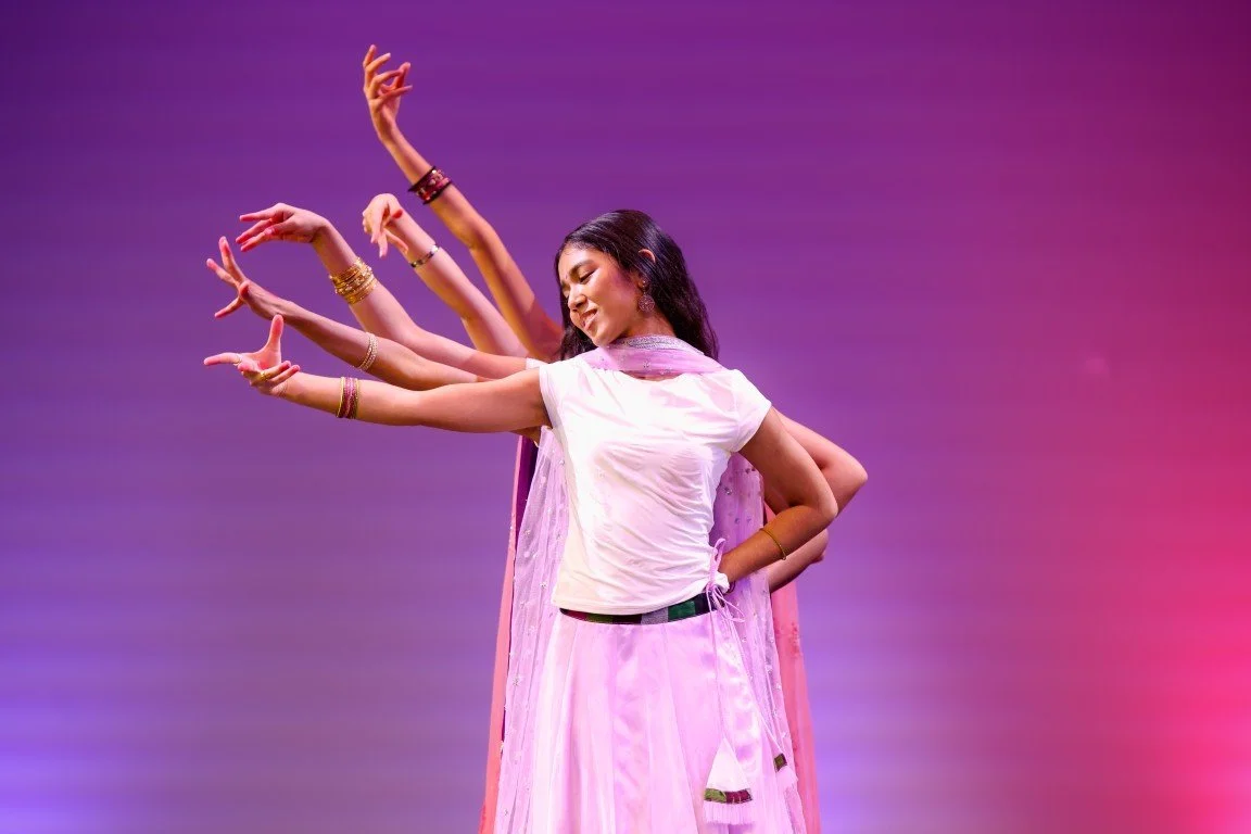 A woman in traditional Indian attire dancing on stage, with multiple arms projected behind her in a layered, artistic display.