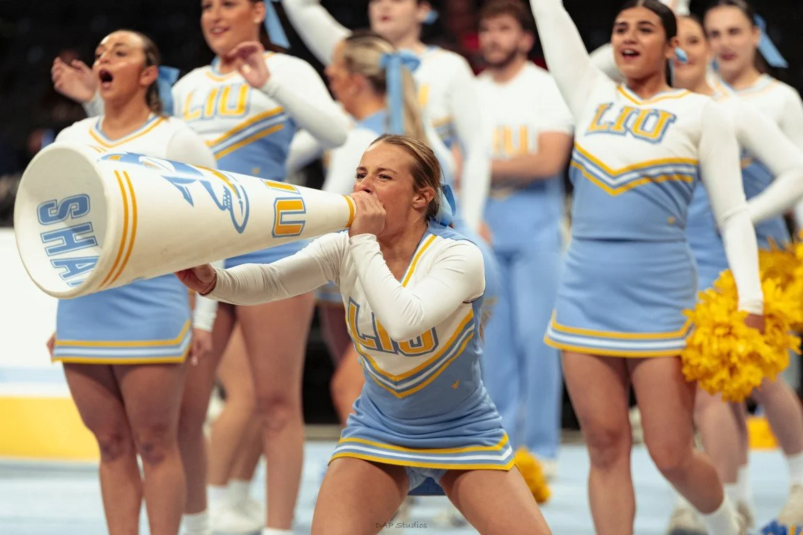 Cheerleaders in LU uniforms cheering on the sidelines during a game, with one cheerleader using a megaphone.