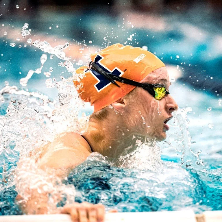 Swimmer wearing an orange cap and goggles swimming in a pool.