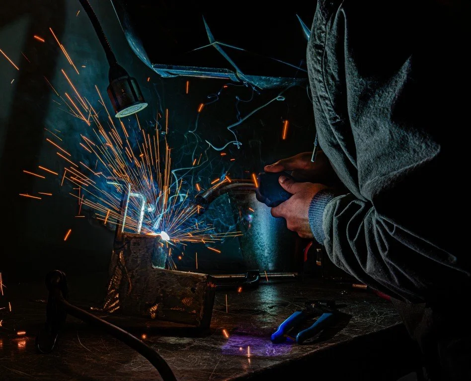 A person welding metal, with sparks flying, in a dark workshop.