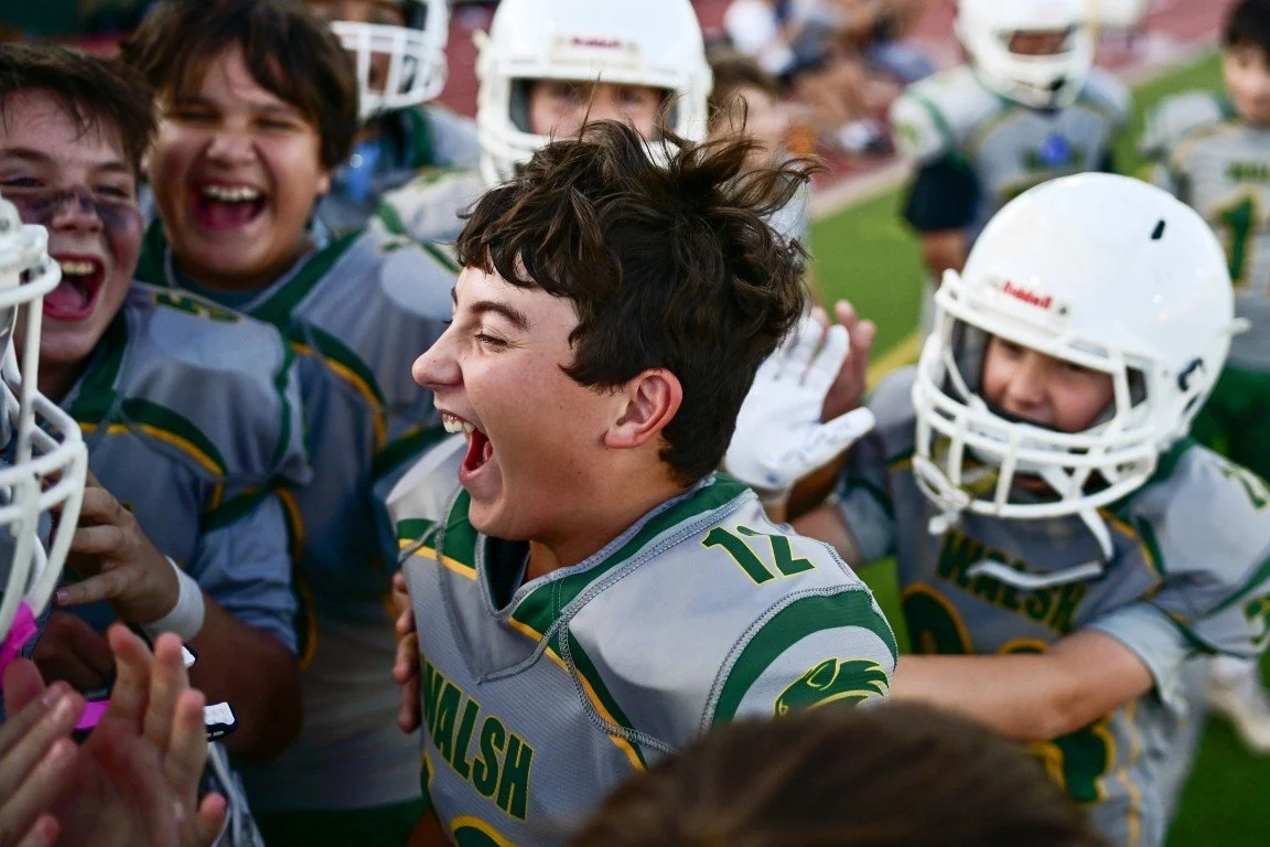 Youth football team celebrating on the field, with players wearing helmets and uniforms, expressing excitement and joy.