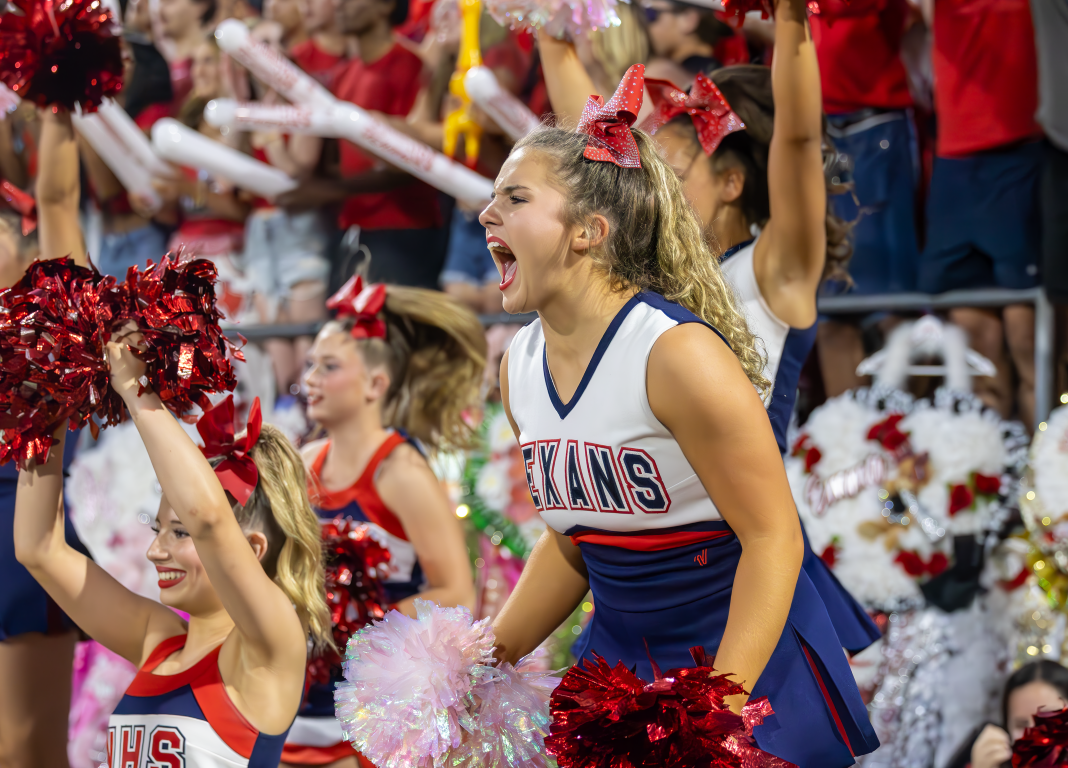 Cheerleaders dressed in red, white, and blue uniforms, performing with pom-poms at a sports event, surrounded by an enthusiastic crowd.