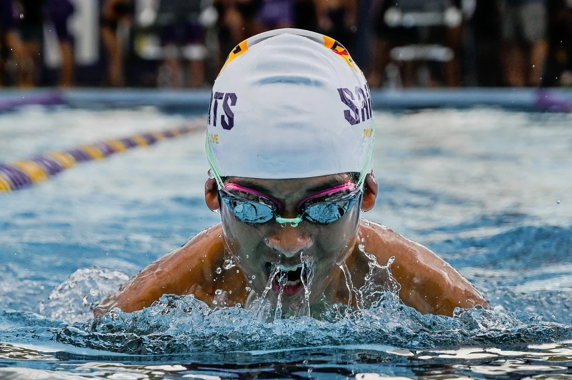 Swimmer in a swimming pool wearing a swimming cap and goggles, taking a breath during a race.