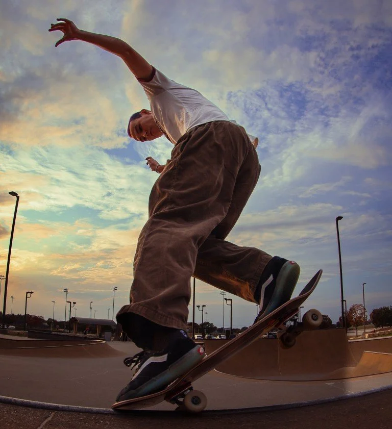 Skateboarder performing a trick on a skateboard at a skatepark during sunset.