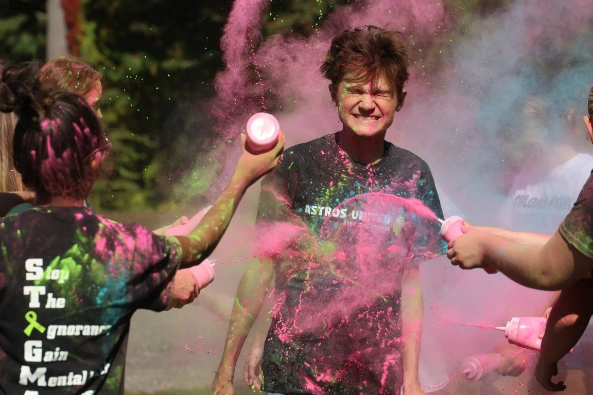 Children celebrate at a color run, throwing colored powder and smiling.
