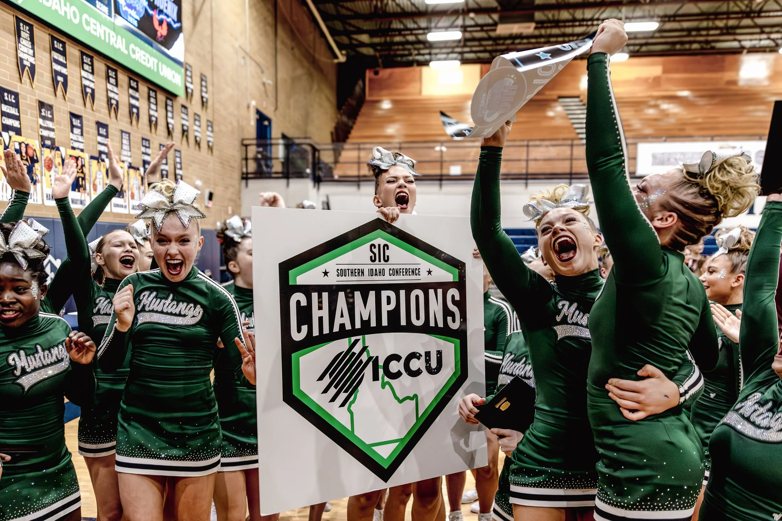 Cheerleaders celebrating with arms raised and shouting, holding a championship sign for Southern Idaho Conference and Midland U.