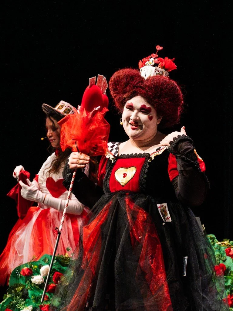 Women dressed as playing cards from the Queen of Hearts deck, with hearts and card-themed accessories, on a stage.