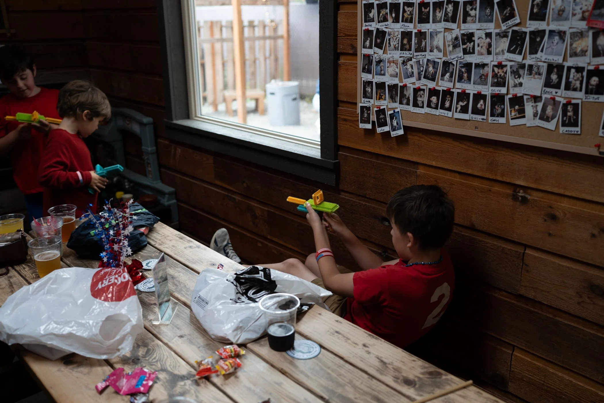 Children in red shirts playing with laser tag guns inside a wooden cabin with a wall of pet photo posters