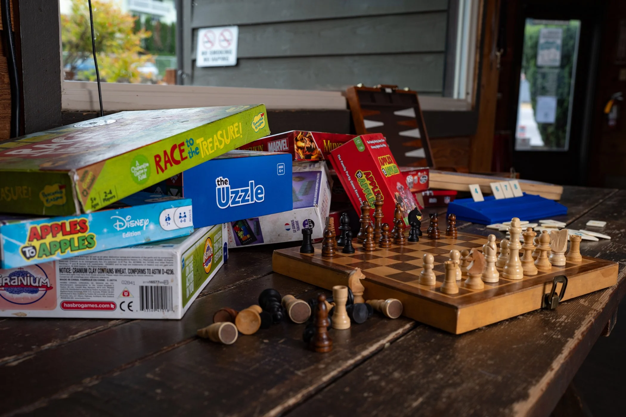 Board game boxes and a chess set on a wooden table inside a rustic building near a window.