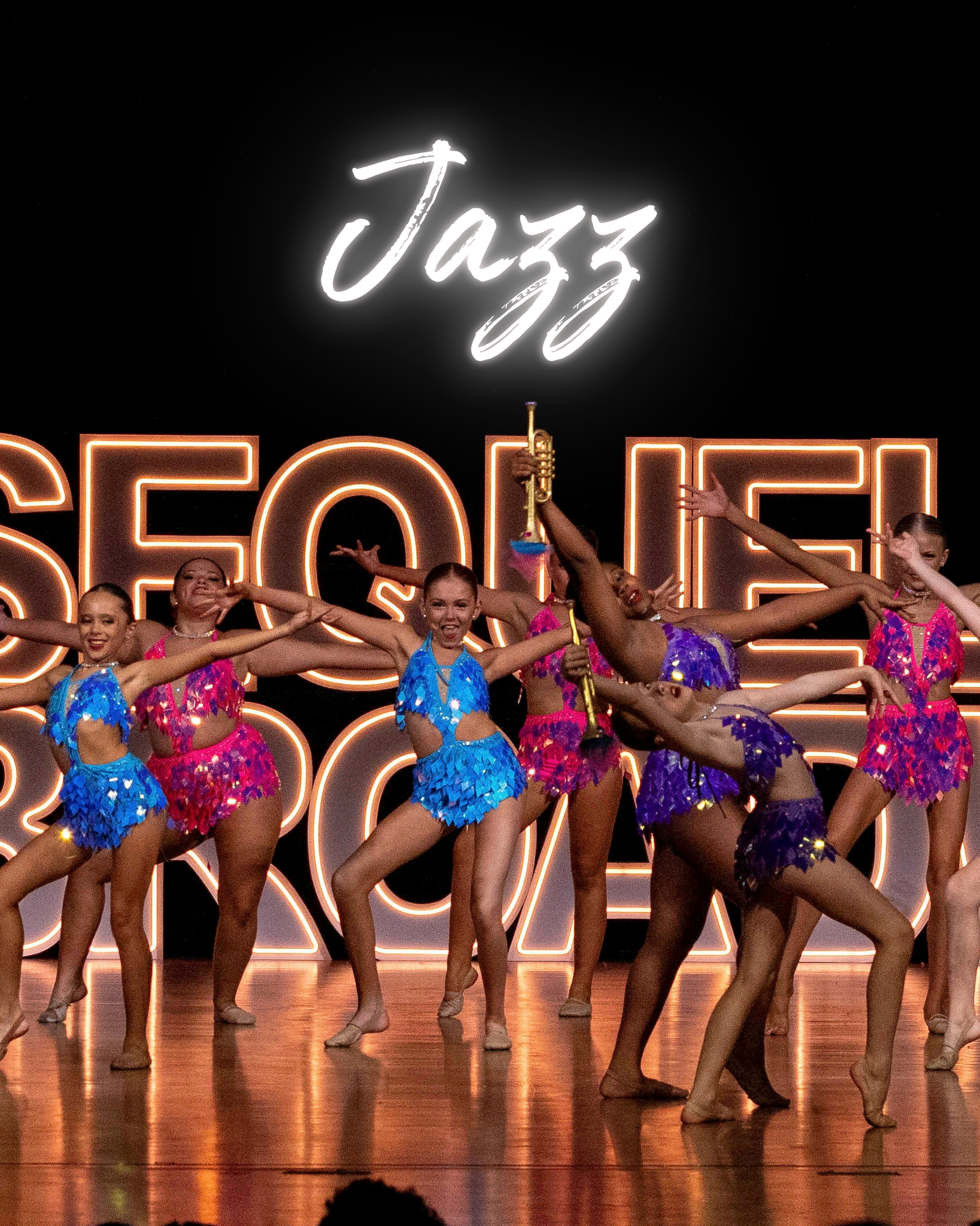 A group of young female dancers performing jazz on a stage in Collierville, TN, wearing colorful costumes and smiling, with a neon sign that says "Jazz" in the background.