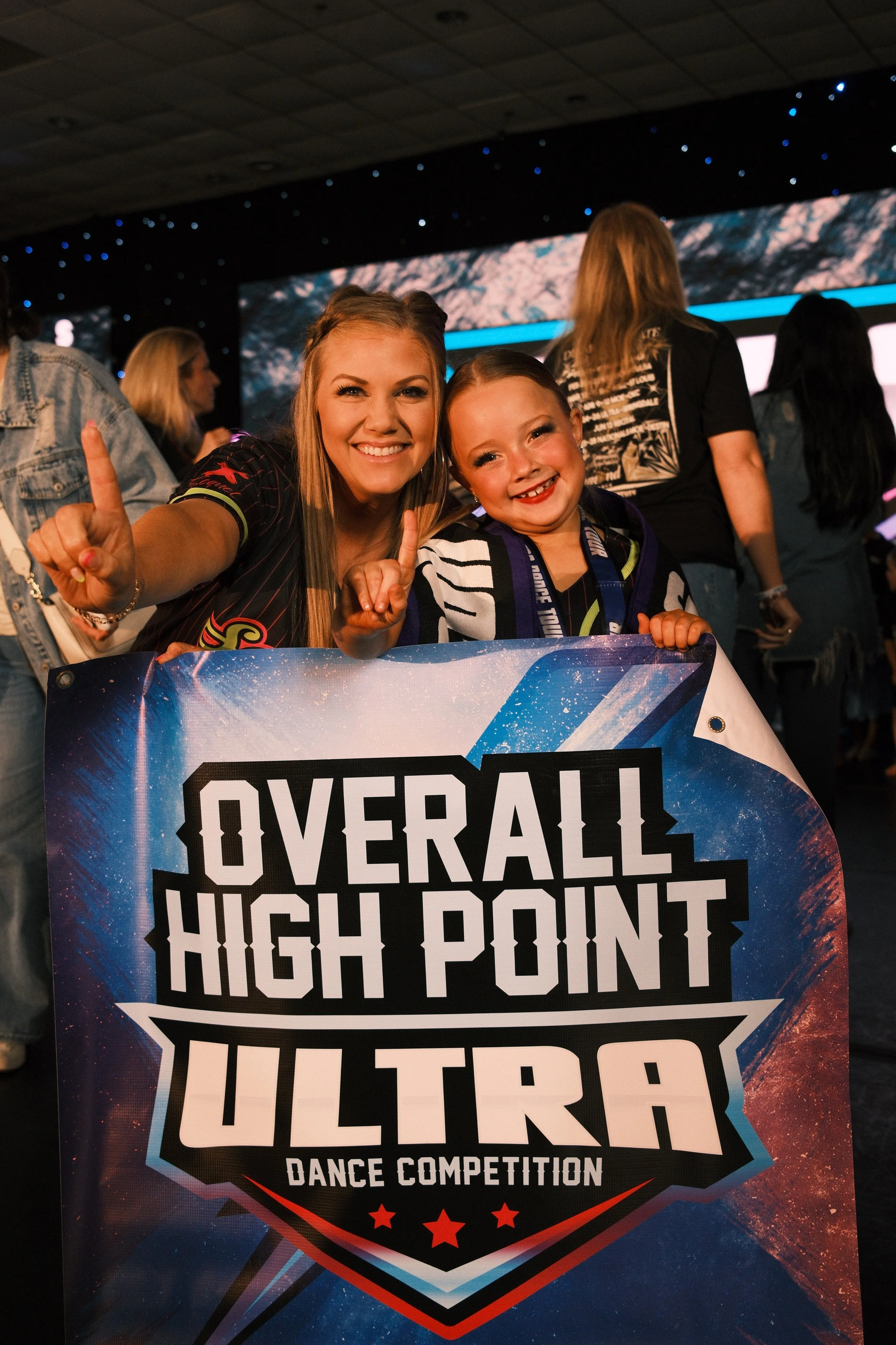 Dance instructor and student smiling and holding a banner for a dance competition with the text "Overall High Point Ultra" at a national dance competition.