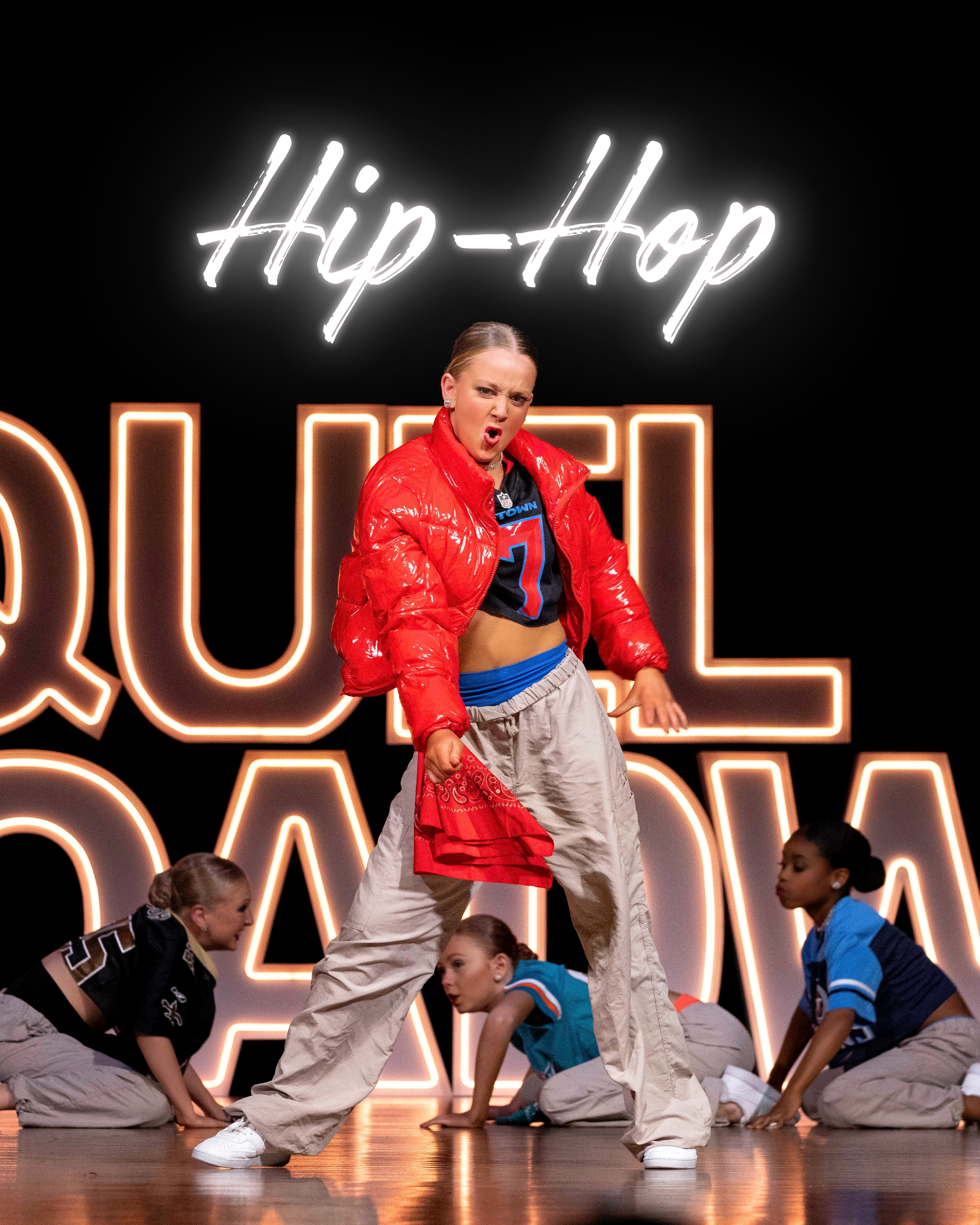 A group of young dancers performing on a stage with a neon sign that reads 'Hip-Hop' in the background. The dancer at the center is a young blonde girl wearing a red jacket, a black shirt, and baggy pants, striking a confident pose. Other dancers are crouching or kneeling around her, dressed in athletic clothes.
