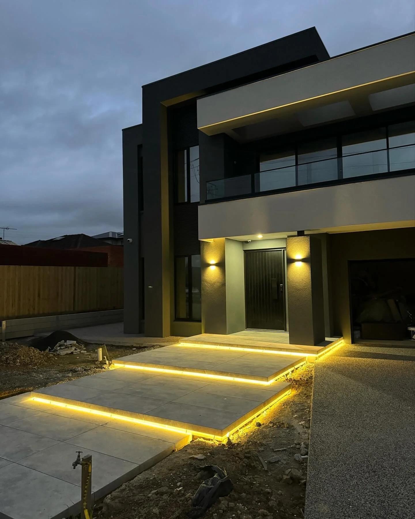 Modern two-story house with illuminated steps and exterior lights at dusk.