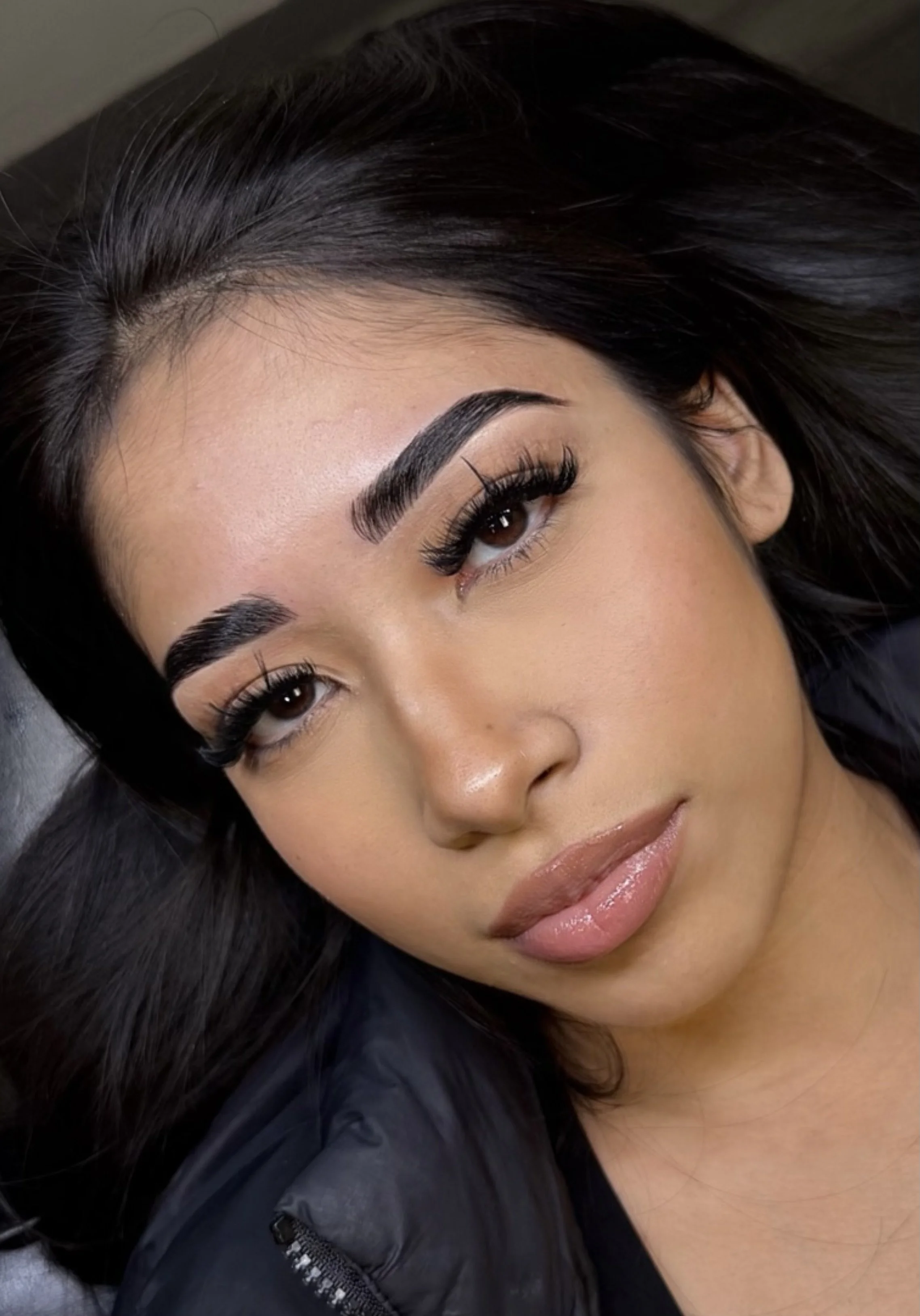 Close-up of a woman's face with dark hair, well-defined eyebrows, long eyelashes, and natural makeup, lying down.