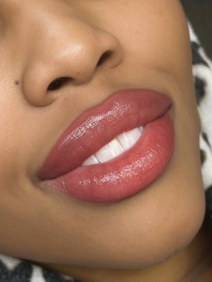 Close-up of a woman's lips slightly parted, showing her white teeth, with glossy lips and smooth skin.