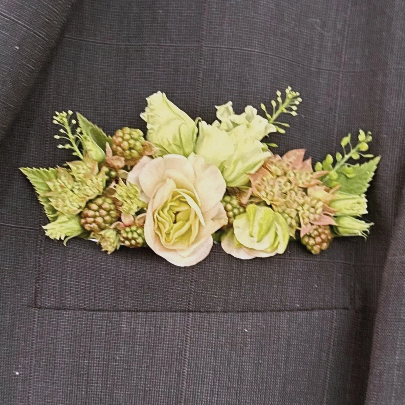 A floral arrangement with white roses, green buds, and assorted greenery placed on a dark gray fabric surface.