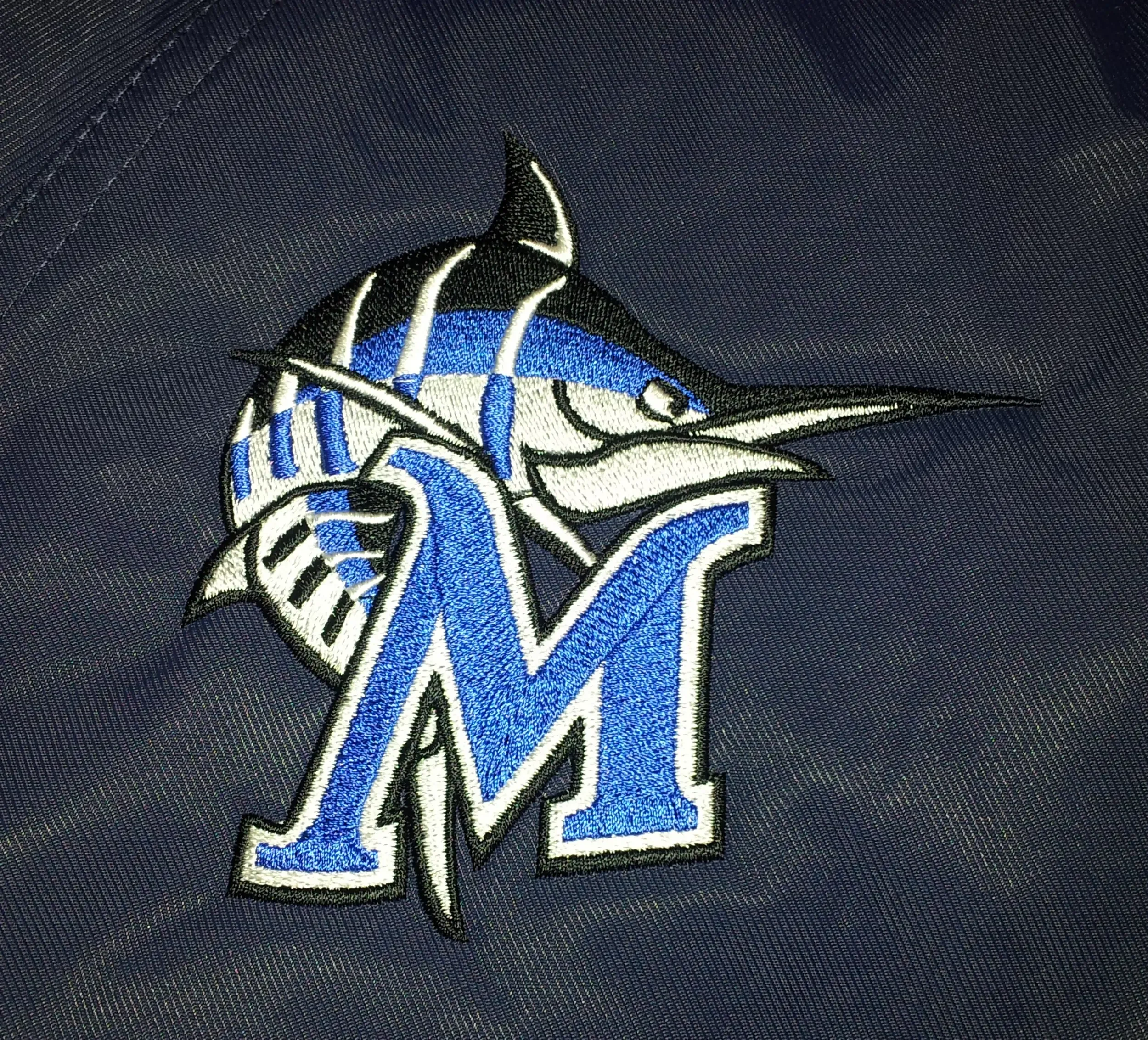 Custom hand digitized Marlin fish logo with styled letter M embroidery on swim jackets and backpacks.