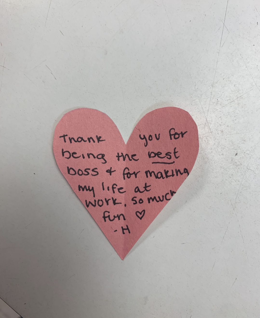 Pink heart-shaped paper with handwritten note expressing gratitude to a boss for making work fun.