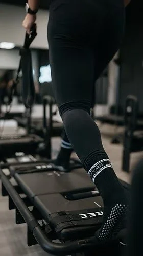 Close-up of a person in black workout leggings on a Lagree machine, holding a resistance cable.