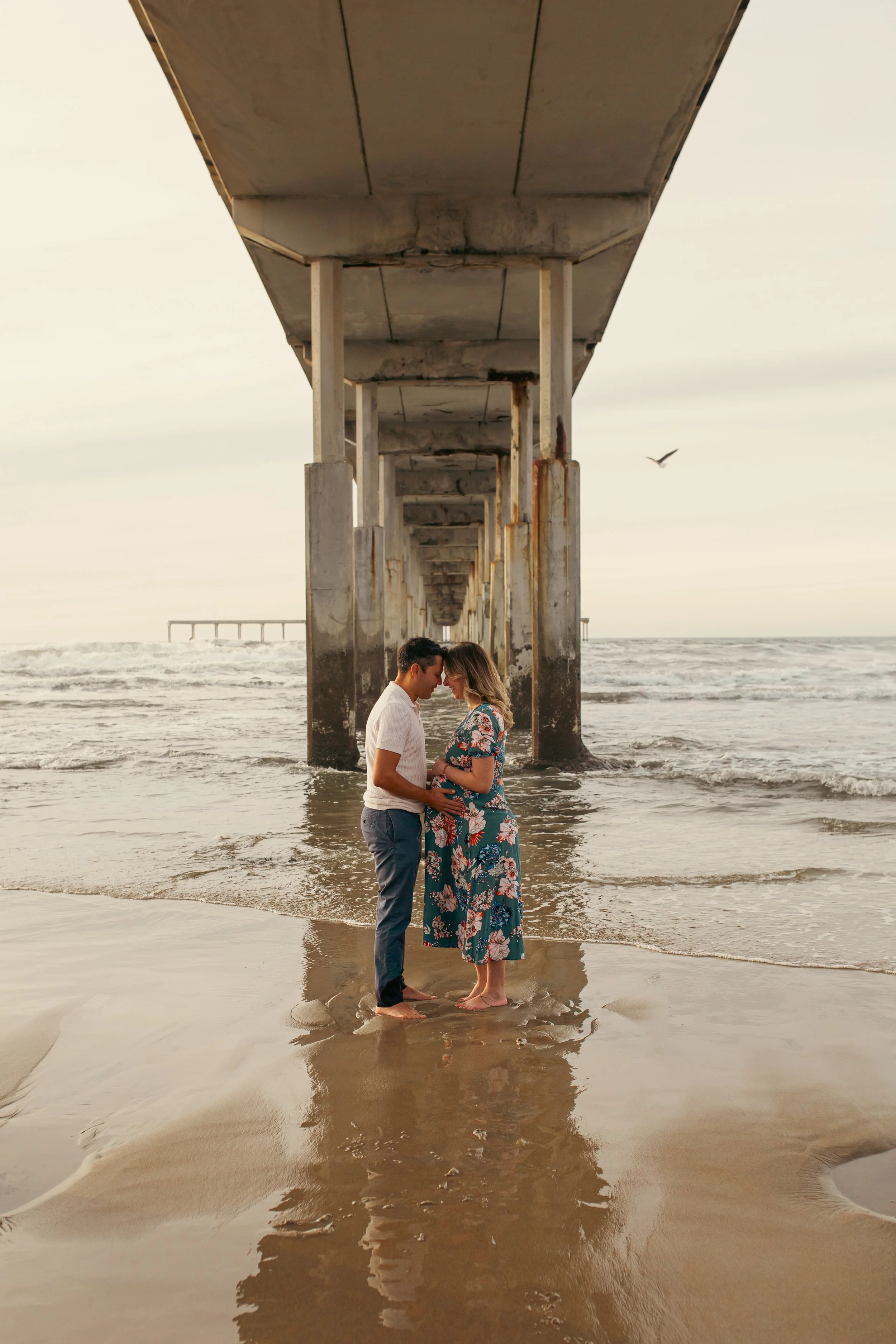 Expecting couple embracing under the OB pier at sunset, Ocean Beach maternity session