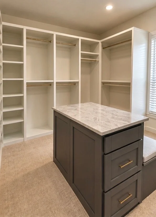 Empty walk-in closet with built-in shelves, hanging rods, and a central island with cabinet drawers and a marble countertop.